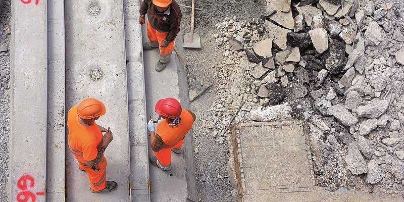 drei Bauarbeiter in orangefarbener Kleidung auf der Baustelle